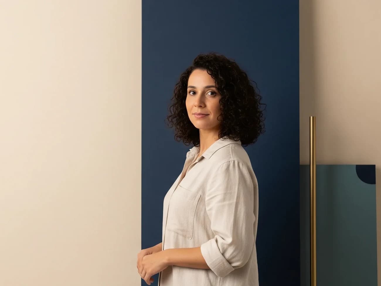 Empreendedora diante do painel navy, do fio de latão e do bloco em verde-mar — a inteligência como instrumento